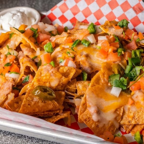 Loaded nachos with melted cheese, diced tomatoes, onions, jalapeños, and a side of sour cream.
