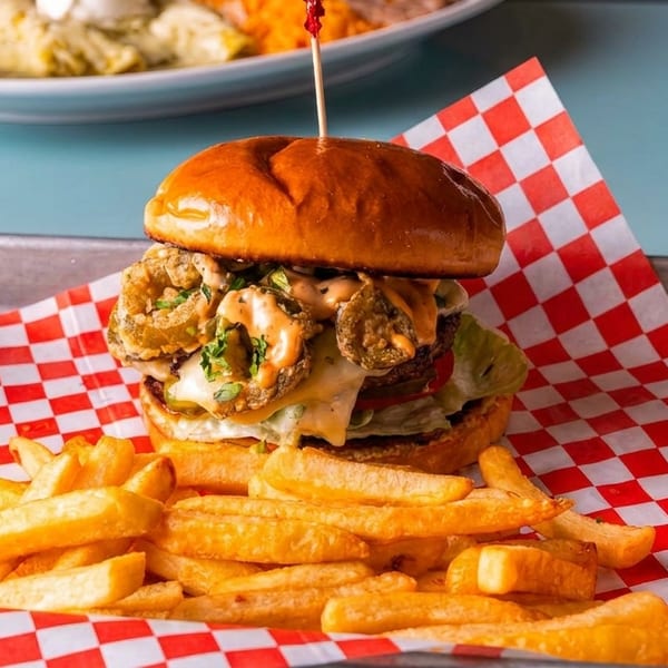 A burger with fried jalapeños and sauce, served with fries on a metal tray with checkered paper.