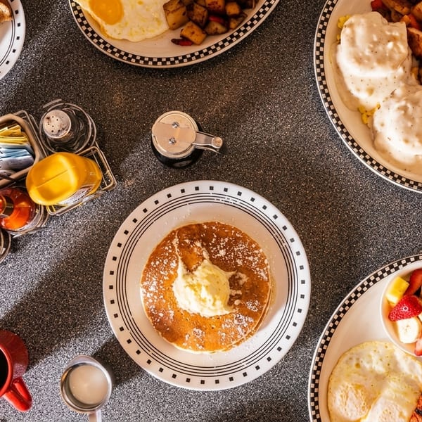 Overhead view of a diner table laden with various breakfast dishes, including pancakes, eggs, and toast.