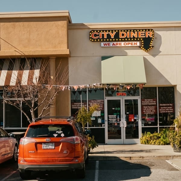 Exterior of City Diner with "We Are Open" sign, two cars parked in front, and clear sky.