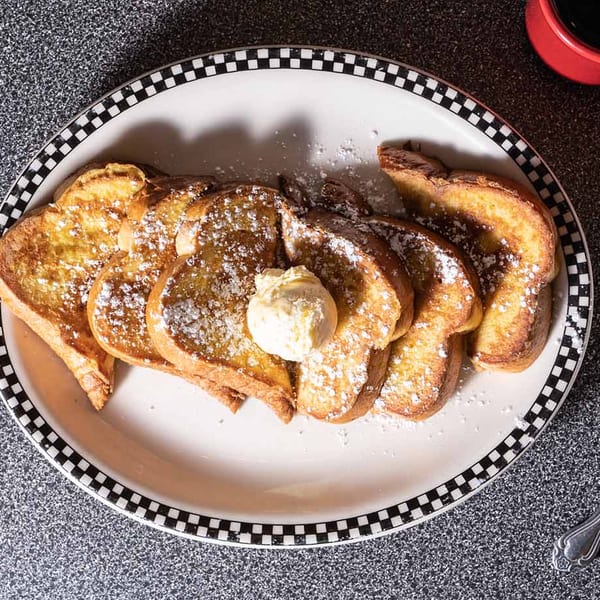 Golden French toast slices, dusted with powdered sugar and topped with butter, on a checkered plate.